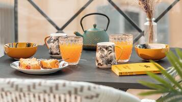 A table with a glass of orange juice, a teapot, and a vase with dried flowers.