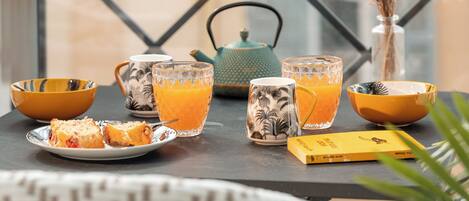 A table with a glass of orange juice, a teapot, and a vase with dried flowers.