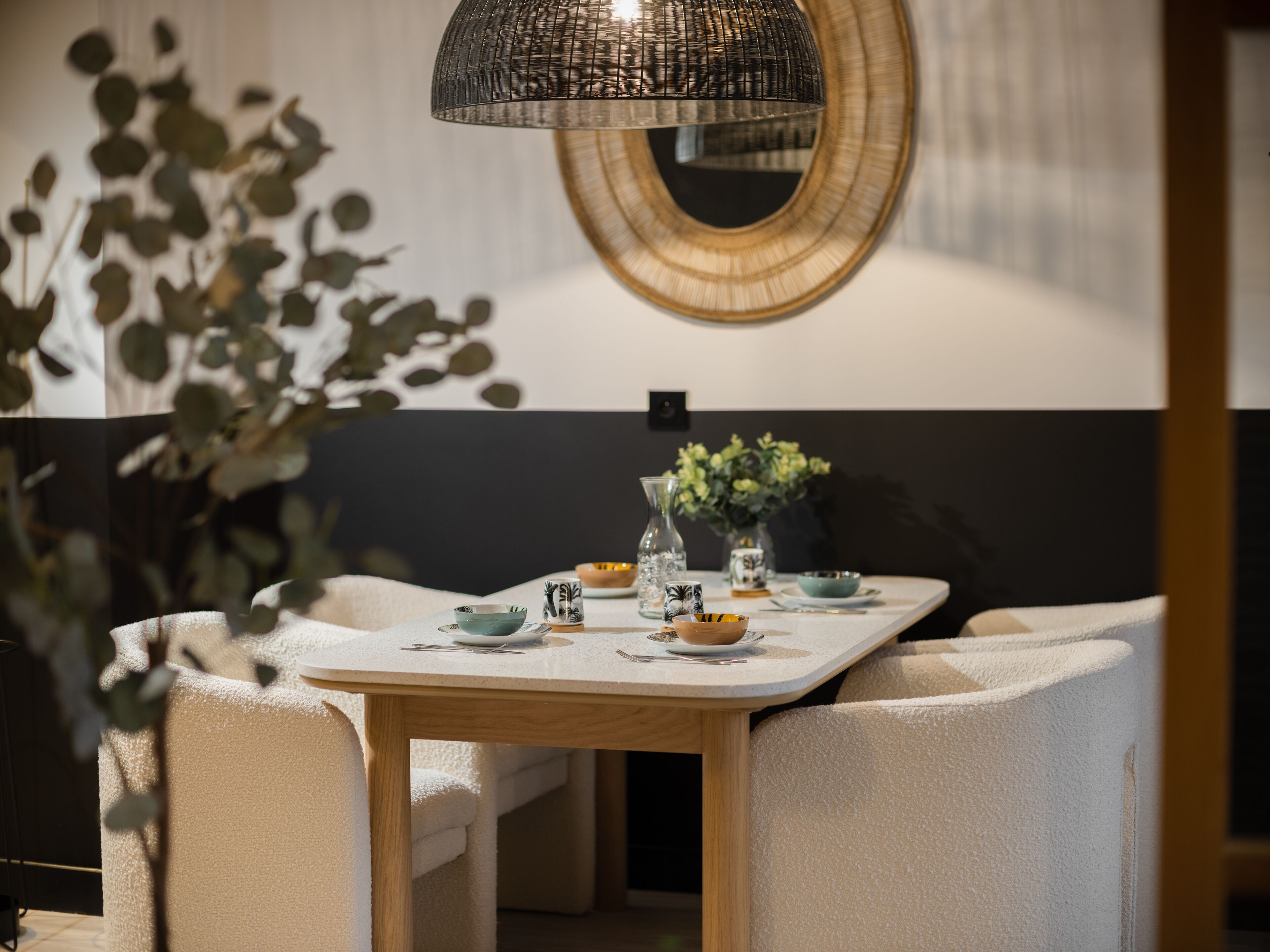 A dining area with a round mirror, a table set with plates, bowls, and a vase of flowers.