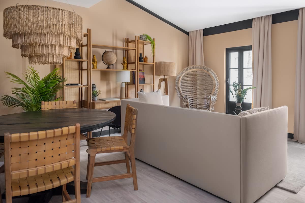 A modern living room with a dining area, featuring a round table, wooden chairs, a sofa, and a large woven chandelier.