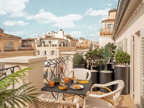 A balcony with wicker chairs, a table with a plate of food, and potted plants. - Maisons du Monde Hôtel & Suites - Marseille Vieux Port (Marseille)