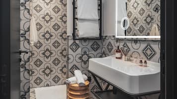 A bathroom with patterned wallpaper, a white sink, a mirror, and a wooden stool.