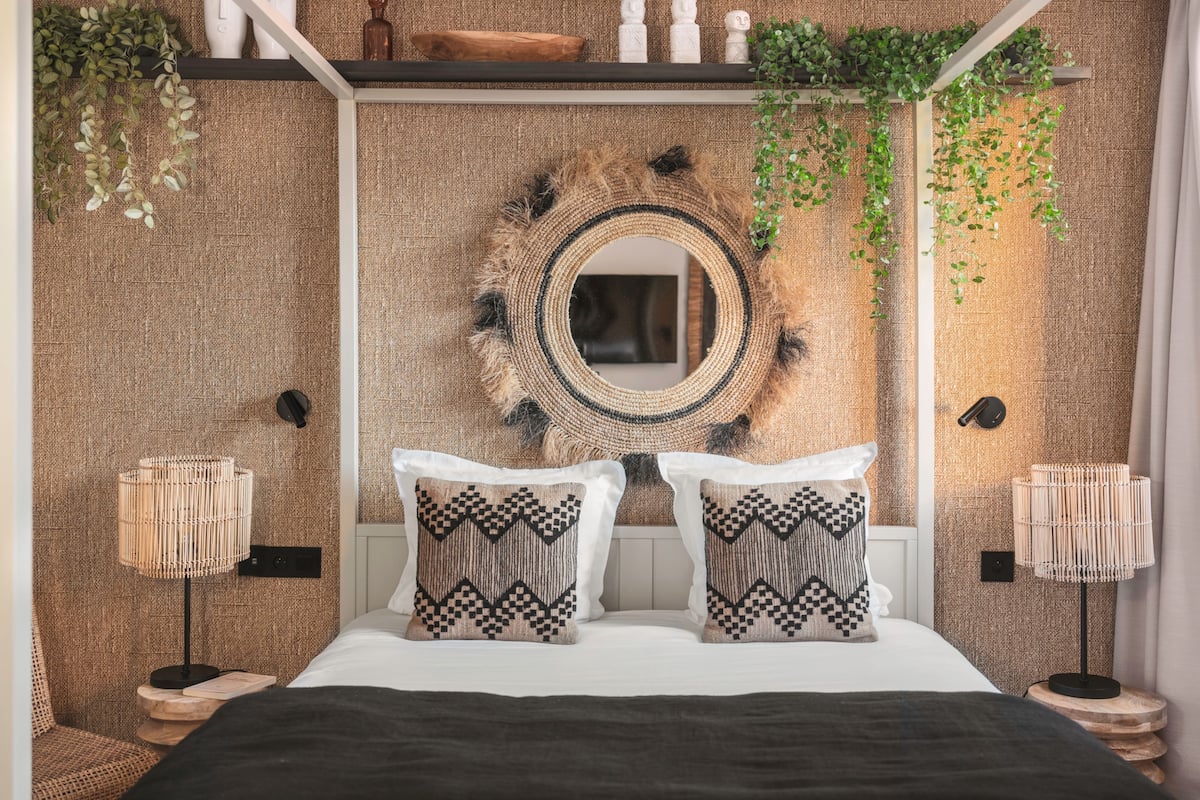 A modern bedroom with a large bed, two patterned pillows, a round mirror, and a textured wall.