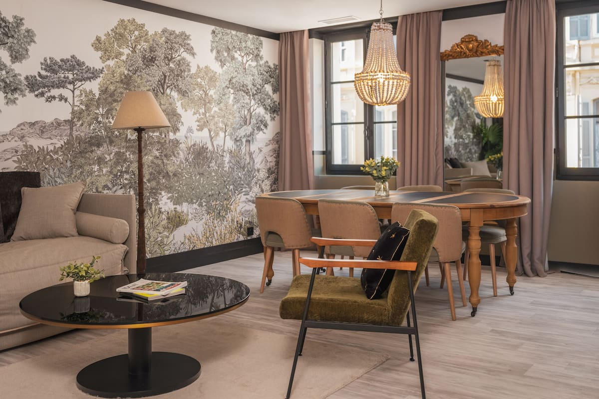 A modern living room with a sofa, a round coffee table, a dining table with chairs, and a chandelier.