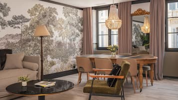 A modern living room with a sofa, a round coffee table, a dining table with chairs, and a chandelier.