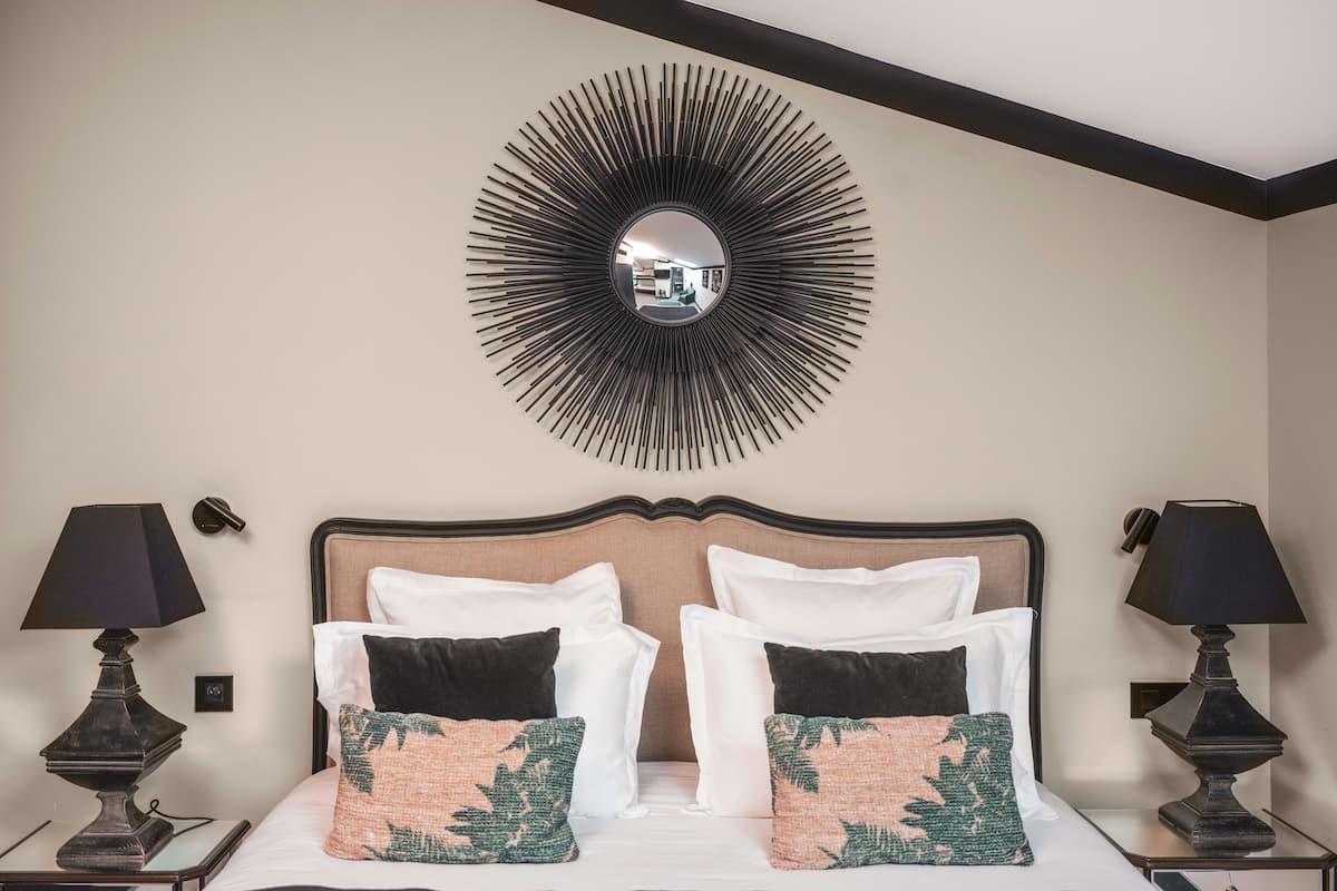 A hotel room with a large bed, two bedside lamps, a wall-mounted mirror, and a decorative wall piece.