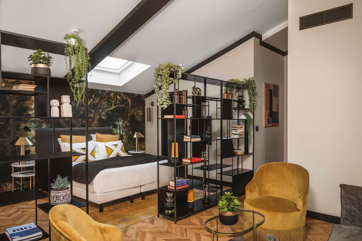 A modern bedroom with a bed, a yellow armchair, a black bookshelf, and a skylight.