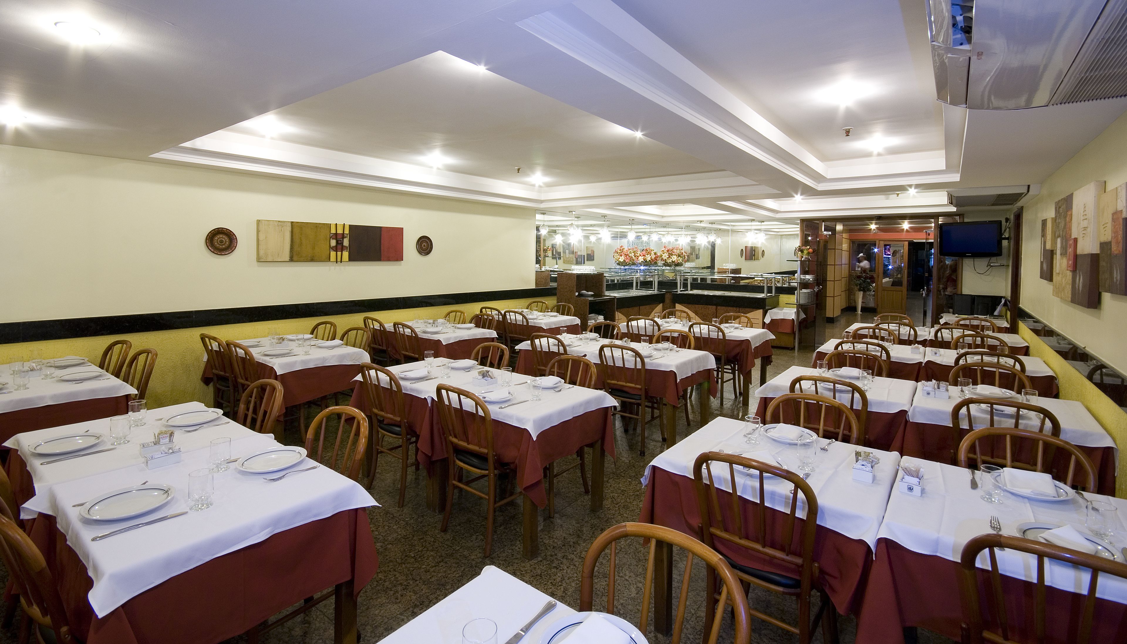 A restaurant with multiple tables set for dining, a buffet area, and a television screen on the wall.