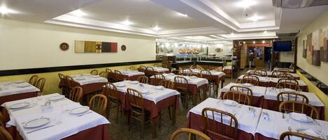 A restaurant with multiple tables set for dining, a buffet area, and a television screen on the wall.
