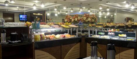 Un área de bufé con diversas opciones de comida, una estación de café y un televisor de fondo.