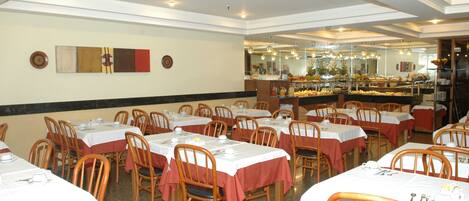 Comedor con varias mesas y sillas, un mostrador de buffet y una pared decorada con platos.