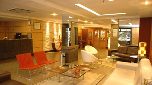 Vestíbulo de hotel con mostrador de recepción, zona de estar con sillas y sofás, y una máquina de café.