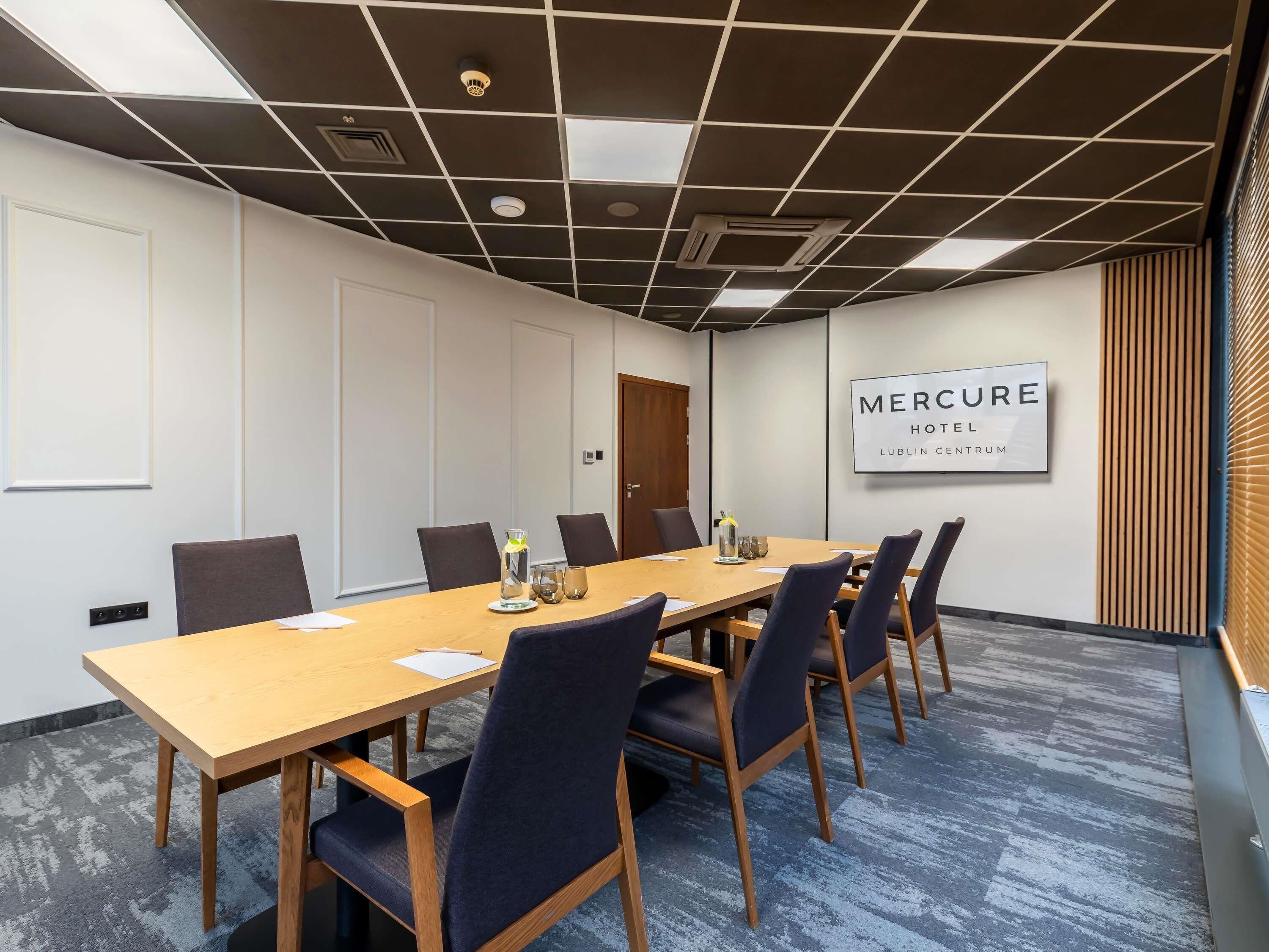 A conference room with a long table, chairs, and a sign reading 'Mercure Hotel Lublin Centrum'.