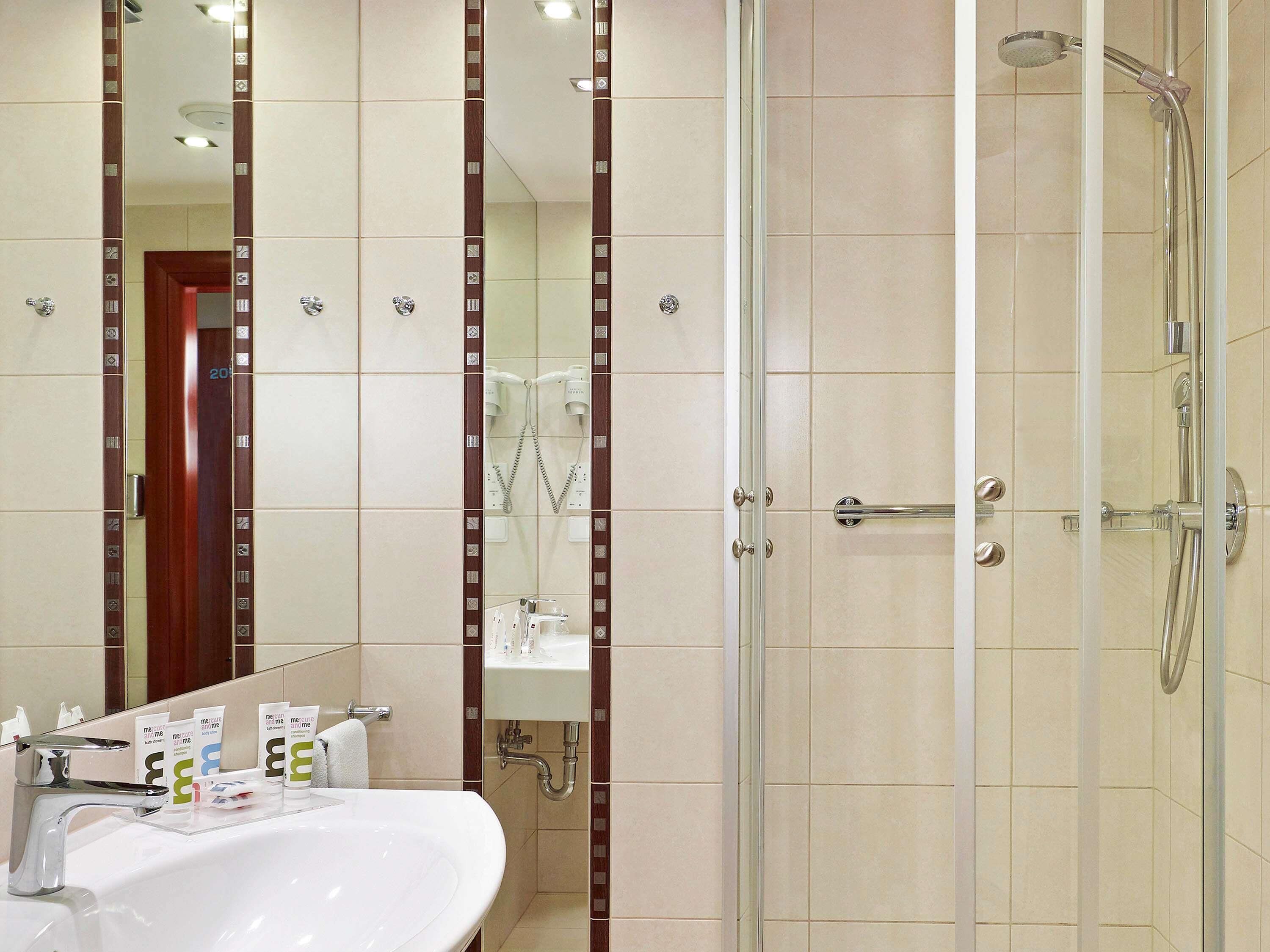 A bathroom with a sink, mirror, shower, and towel rack.
