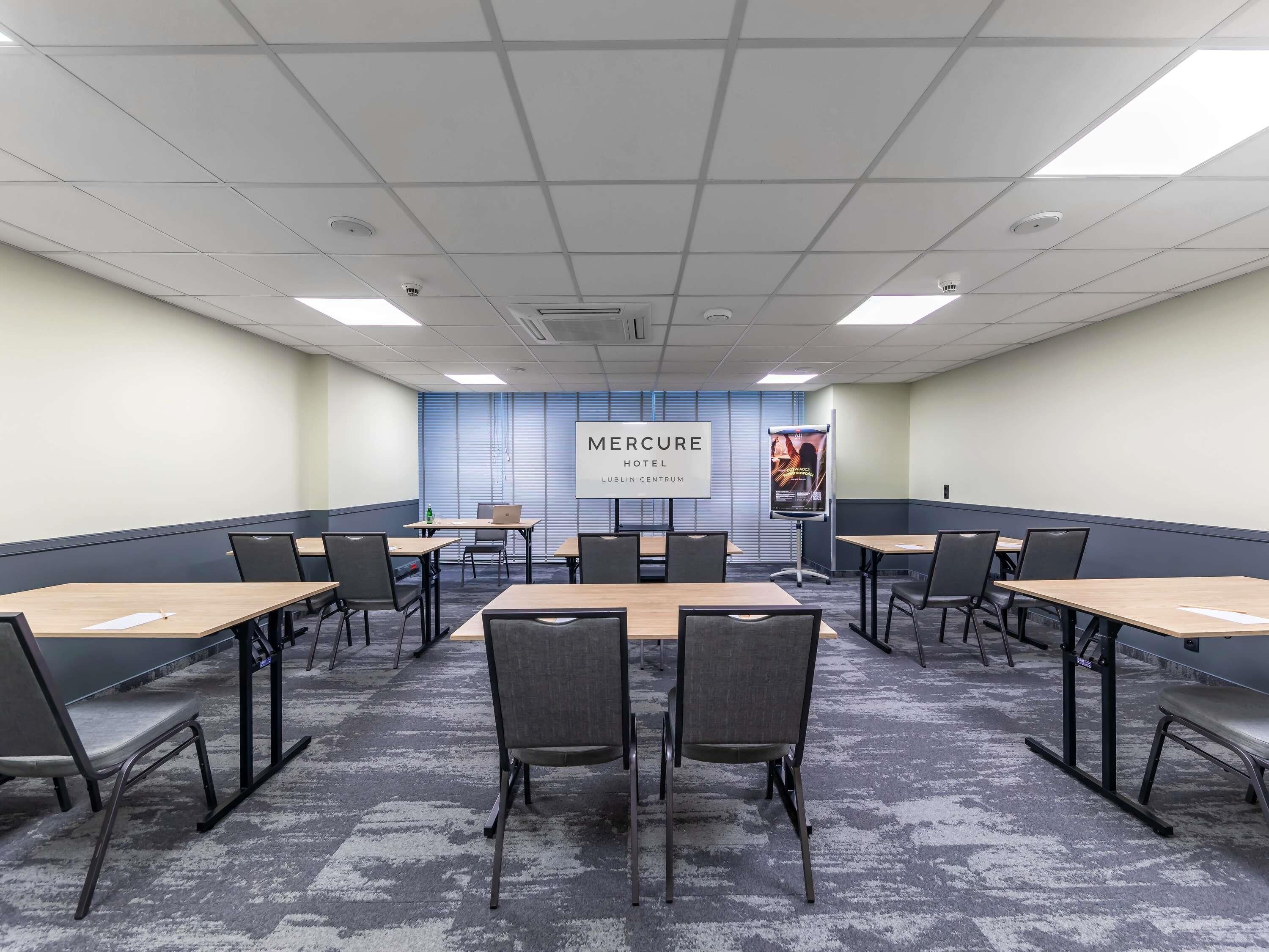 Un salón de conferencias con una amplia mesa, sillas, una computadora portátil y un cartel en la pared.