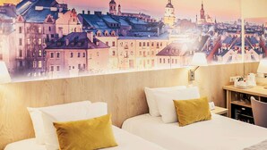 A hotel room with two beds, a wooden headboard, a nightstand with a lamp, and a cityscape view. - Hotel Mercure Lublin Centrum (Lublin)