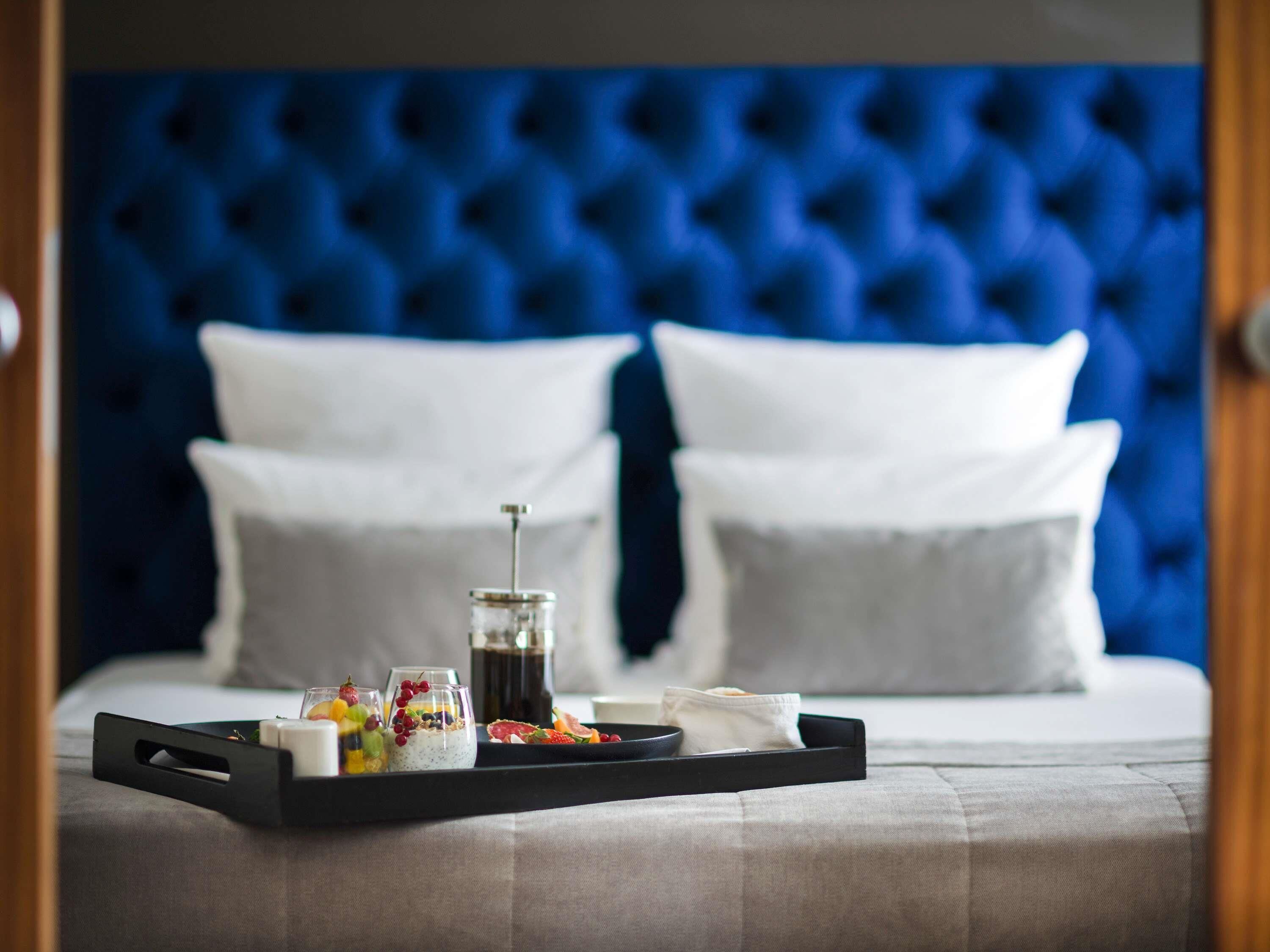 A neatly made bed with a blue tufted headboard, white pillows, and a tray with breakfast items.