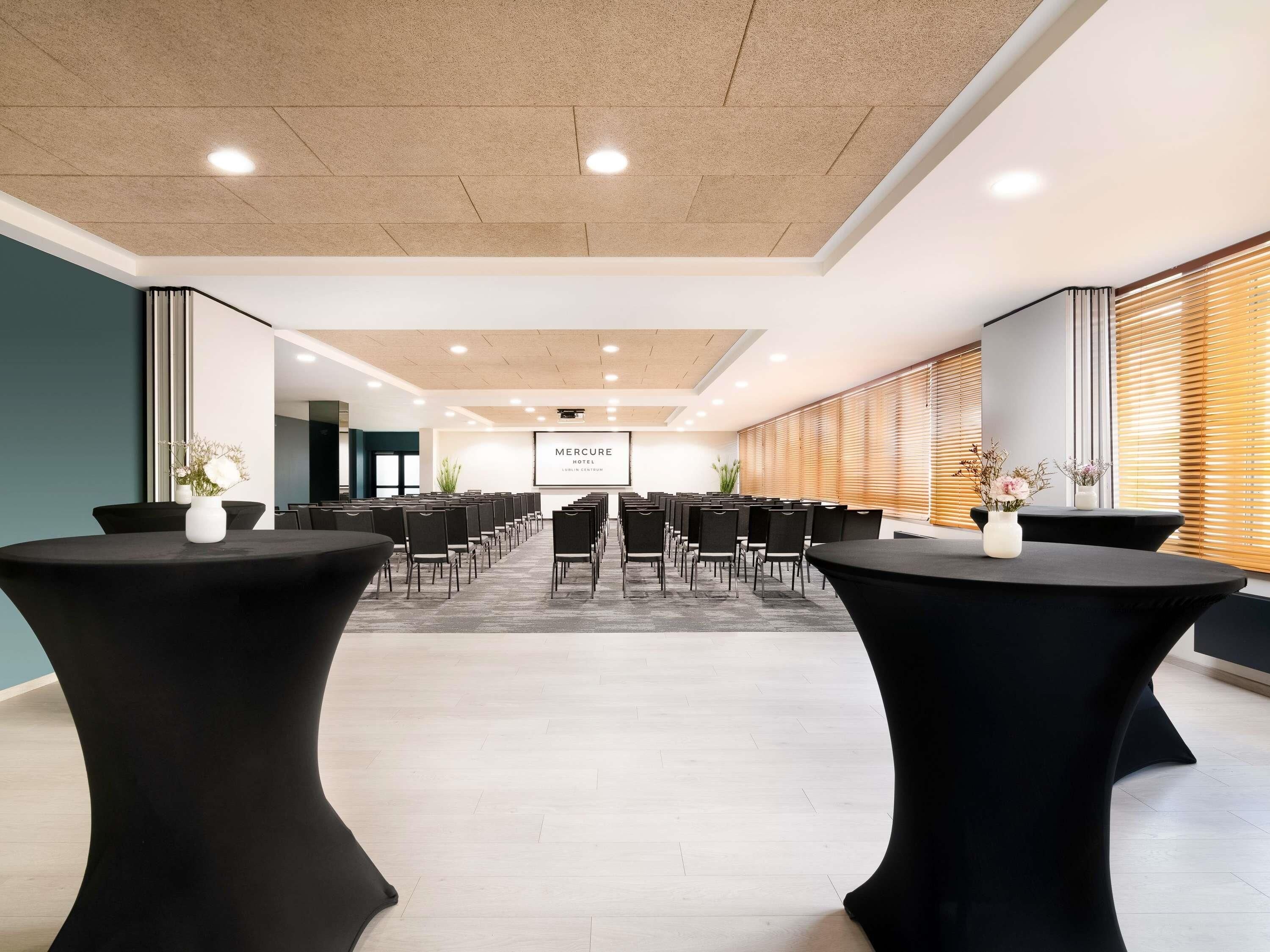 Una sala de conferencias con una larga mesa y sillas, una pantalla grande y una pared de madera con persianas.