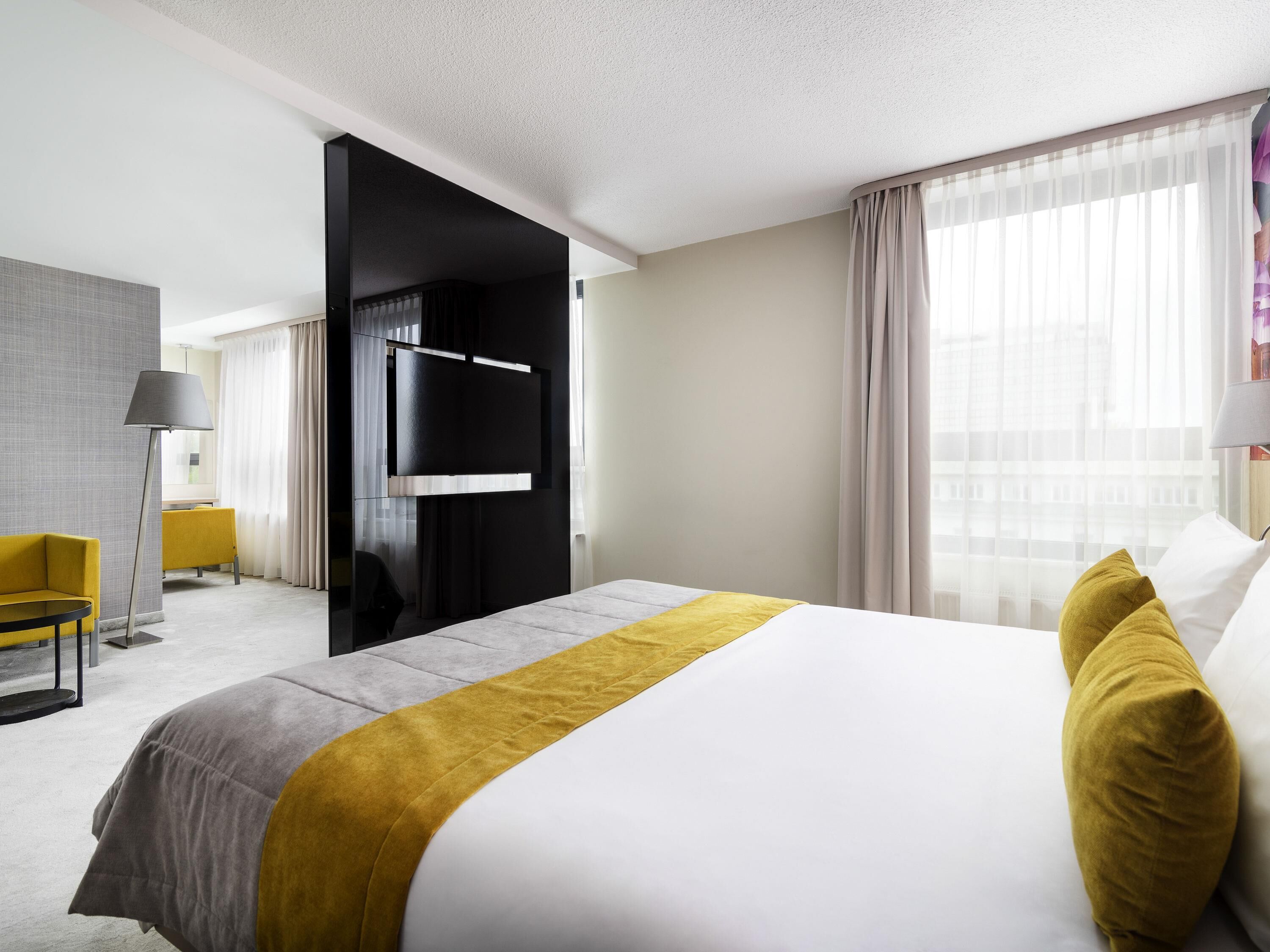 A hotel room with a bed, a desk, a chair, a TV, and a window with curtains.