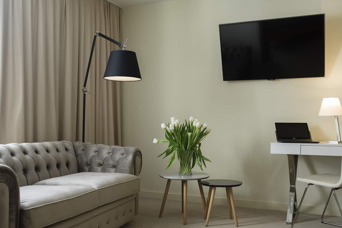 A modern living room with a tufted sofa, a flat-screen TV, a desk with a laptop, a lamp, and a vase with white flowers.