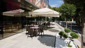 An outdoor seating area with tables and chairs, a large mural on the building, and a white umbrella providing shade. - Hotel Mercure Lublin Centrum (Lublin)