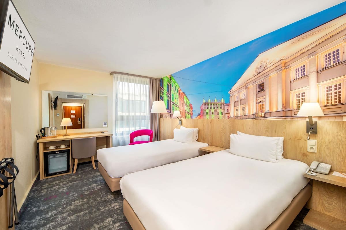 Une chambre d’hôtel avec deux lits, un bureau, une chaise, un miroir et une fresque murale.