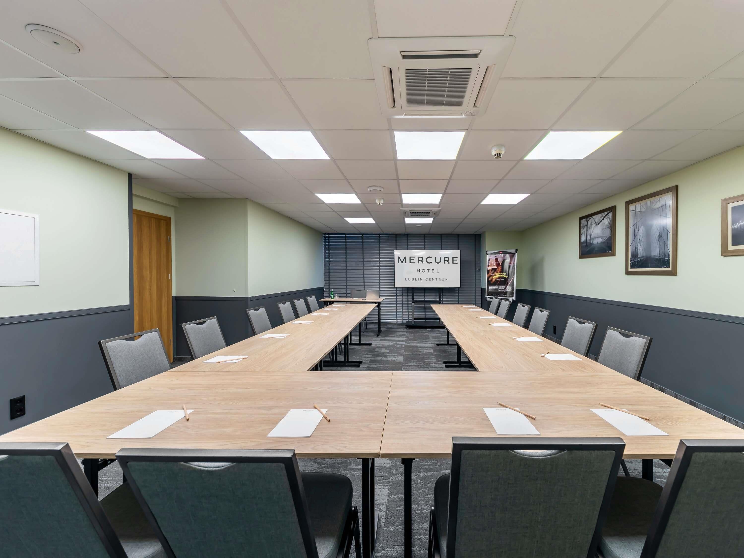 A conference room with a long table, chairs, ceiling lights, and a sign for Mercure Hotel.