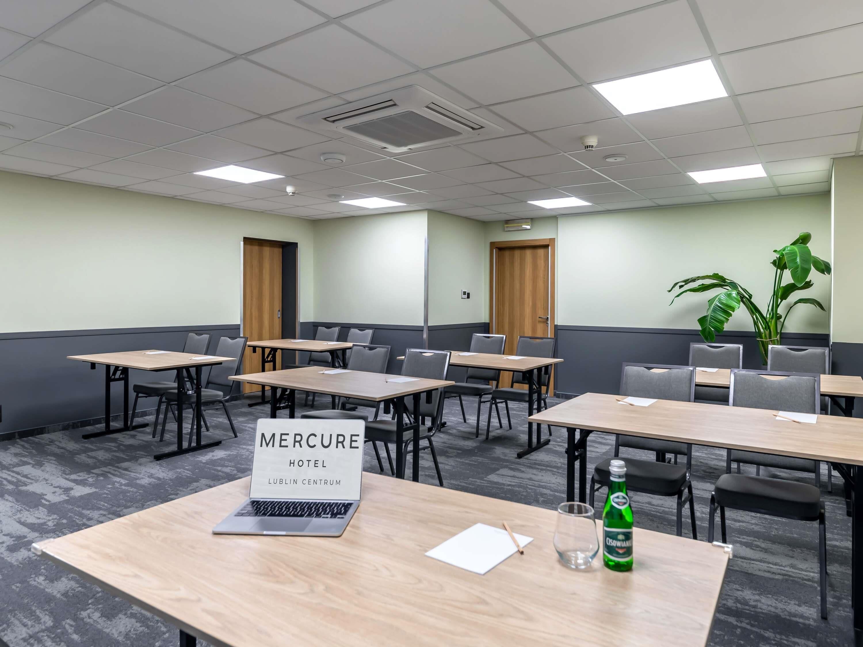 Un salón de conferencias con mesas, sillas, una computadora portátil, una botella y un cartel que indica que es el Hotel Mercure Lublin Centrum.