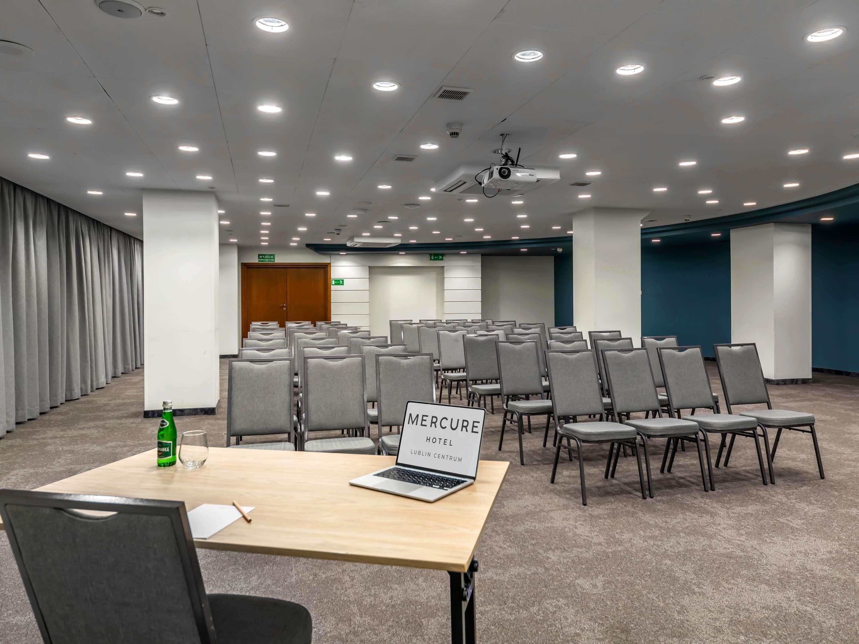 Ein Konferenzraum mit Reihen von Stühlen, einem Laptop auf einem Tisch und einem Projektor.