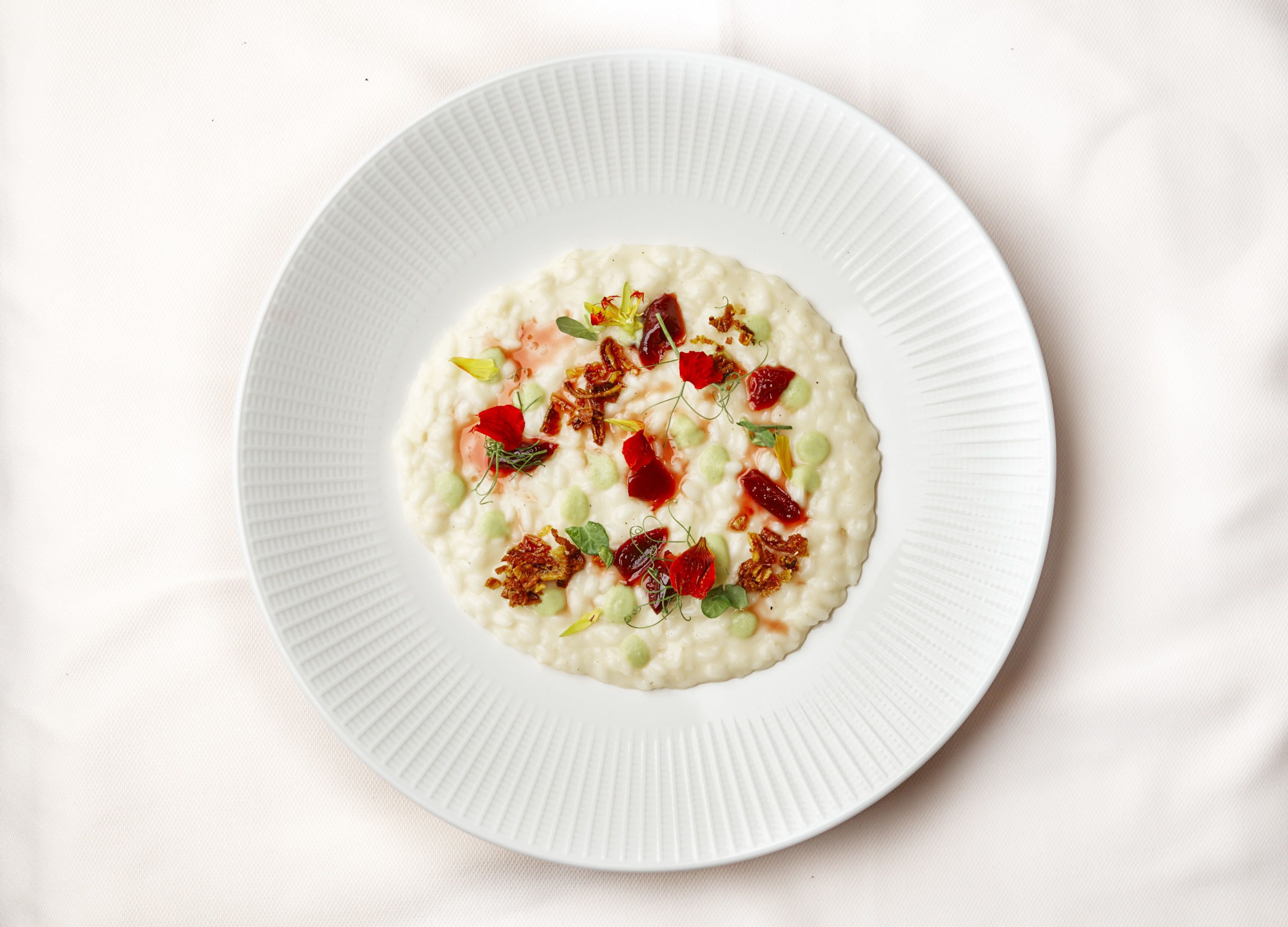 Un plato blanco con un guiso cremoso adornado con bayas rojas, guisantes verdes y nueces.