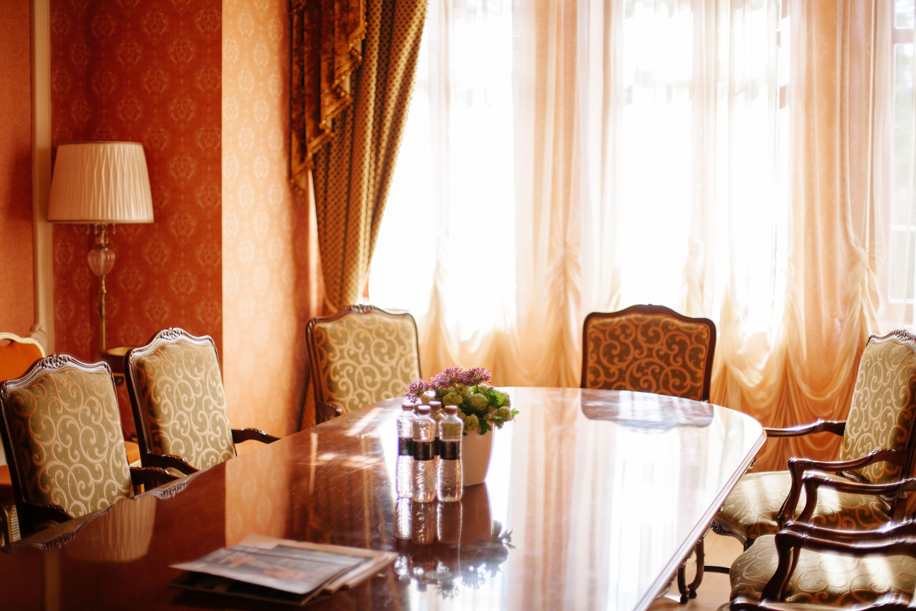Un salón de conferencias con una gran mesa ovalada, seis sillas tapizadas, un centro de mesa floral y una lámpara.