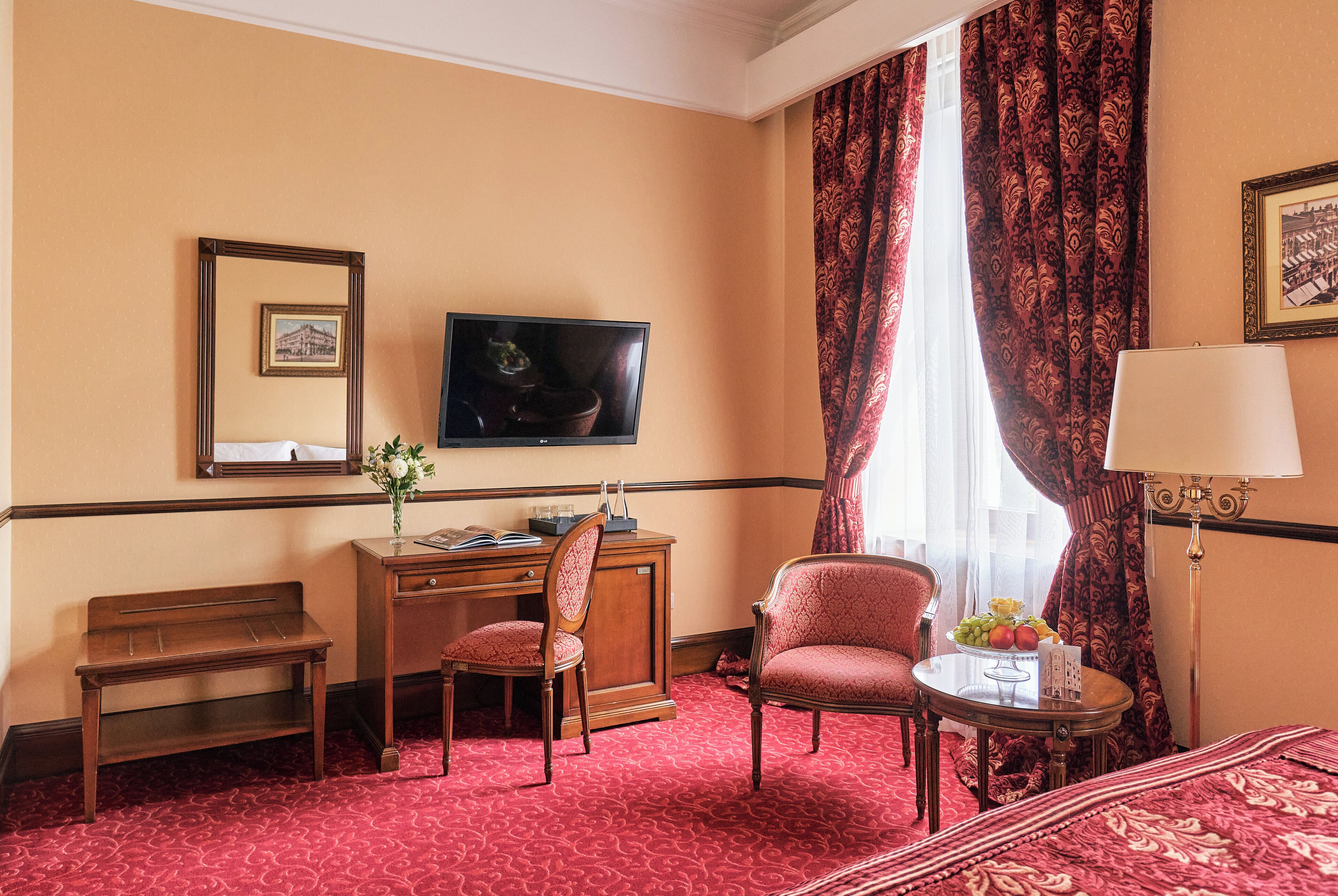 A hotel room with a bed, a desk with a chair, a television, a lamp, and a window with curtains.