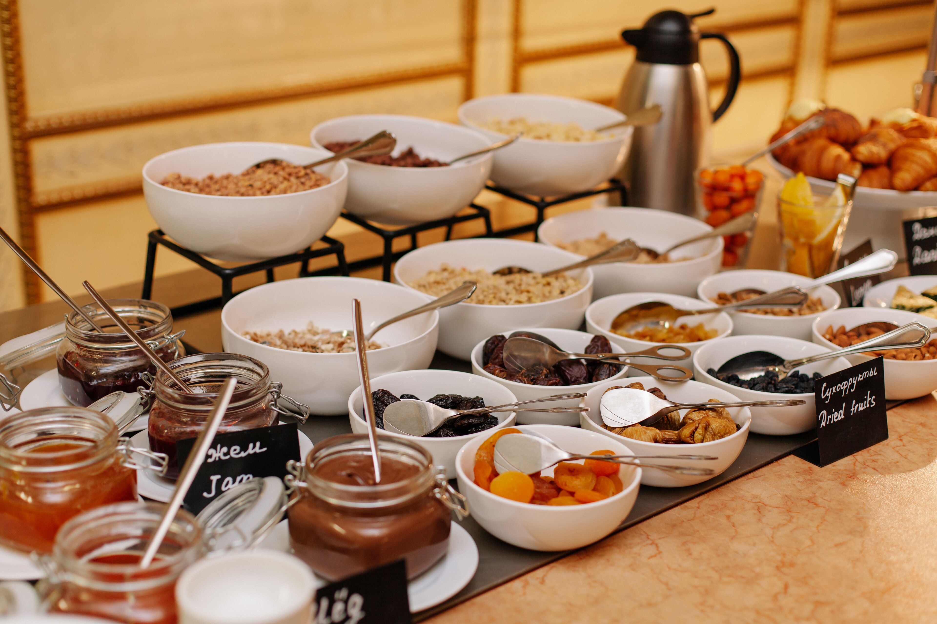 Un bufé con diversos alimentos, incluyendo frascos de mermelada, tazones de cereales y frutas secas.