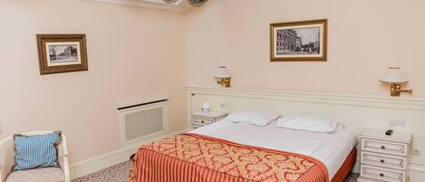 A hotel room with a large bed, two bedside tables, a chair, and two wall-mounted lamps.