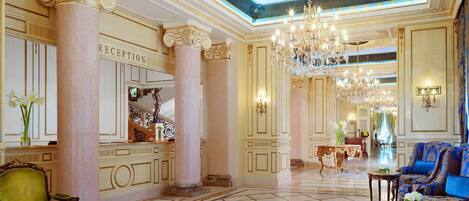 Un'imponente hall con colonne in marmo, una reception, lampadari sfarzosi e confortevoli posti a sedere.