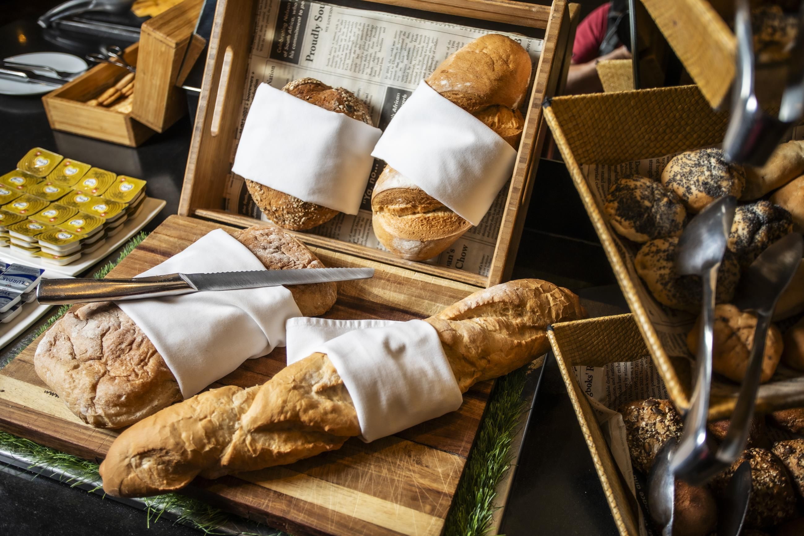 Une variété de pains et de viennoiseries présentés sur des planches en bois et dans un panier, avec un journal en dessous.