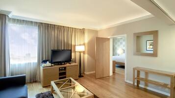 Een hotelkamer met een flatscreen televisie, koffiezetapparaat, lamp, bank, een klein tafeltje en een bed.
