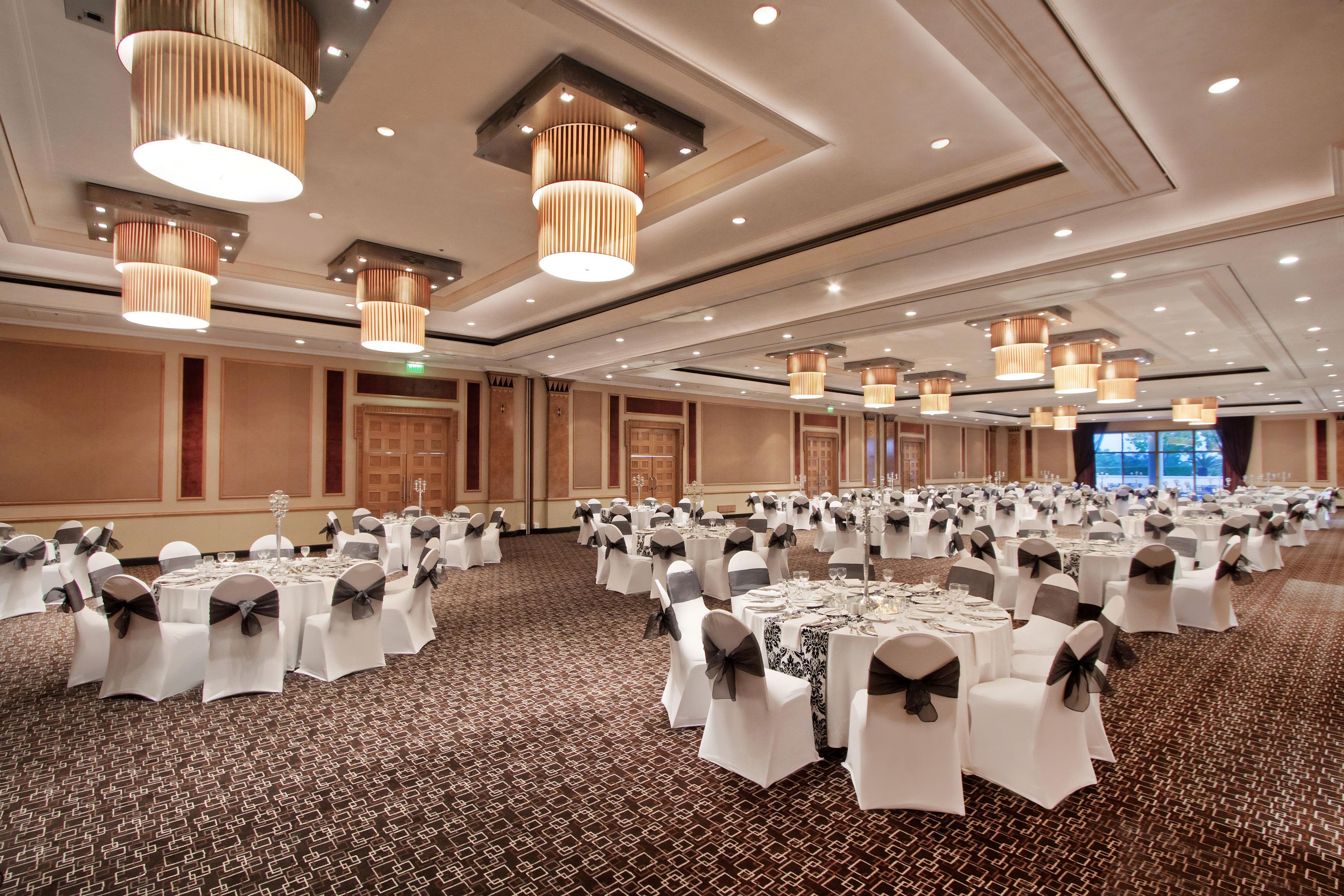 A large banquet hall with round tables set for events, featuring a patterned carpet and modern lighting fixtures.