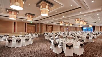 A large banquet hall with round tables set for events, featuring a patterned carpet and modern lighting fixtures.
