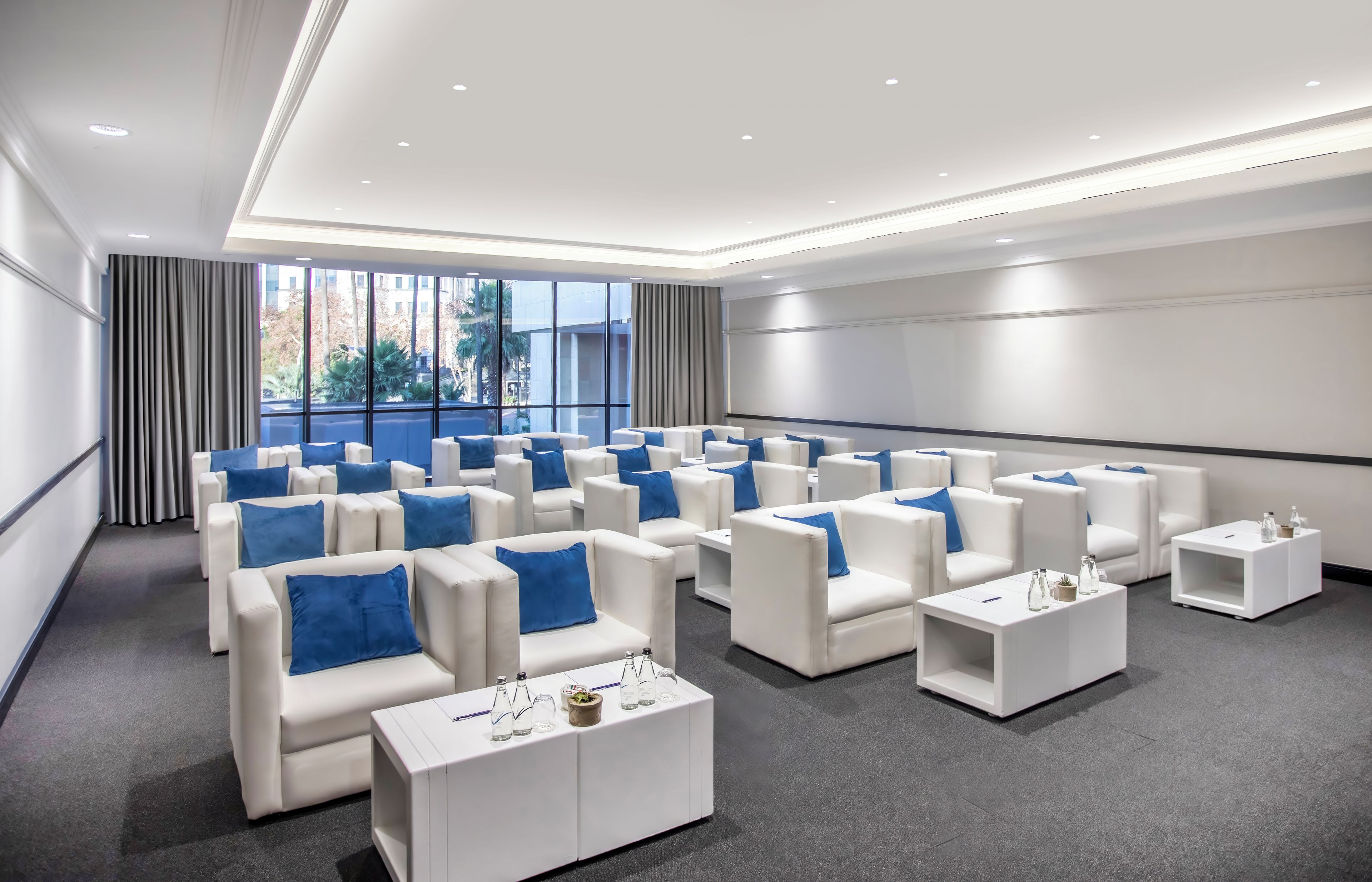 A conference room with rows of white chairs, a large screen, and a view of buildings outside.