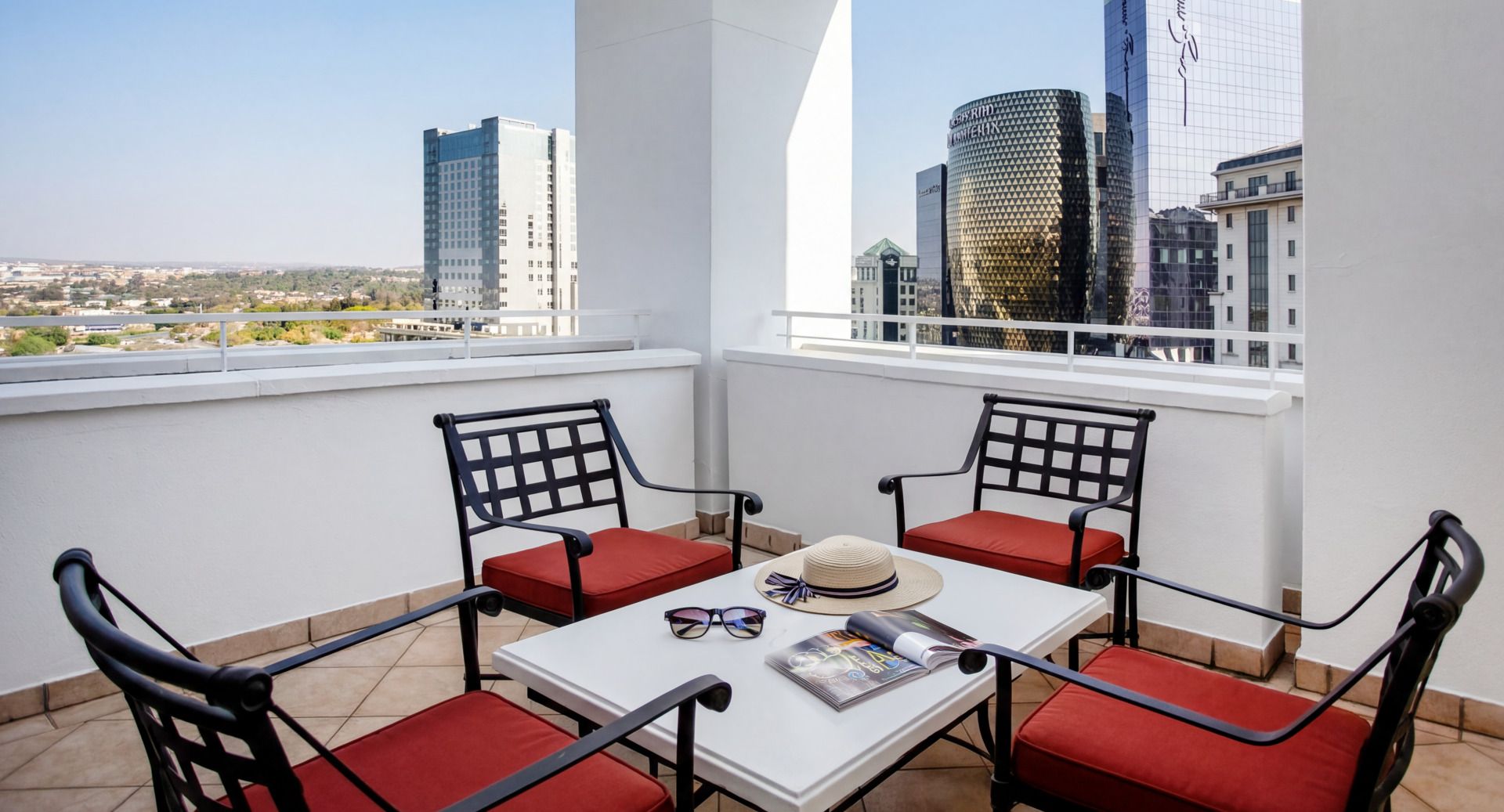 A balcony with a table and chairs, a hat, and sunglasses on the table.