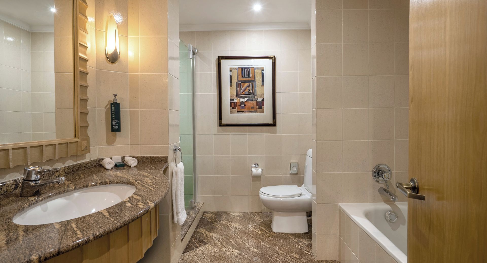 A bathroom with two sinks, a toilet, a bathtub, and a framed artwork on the wall.