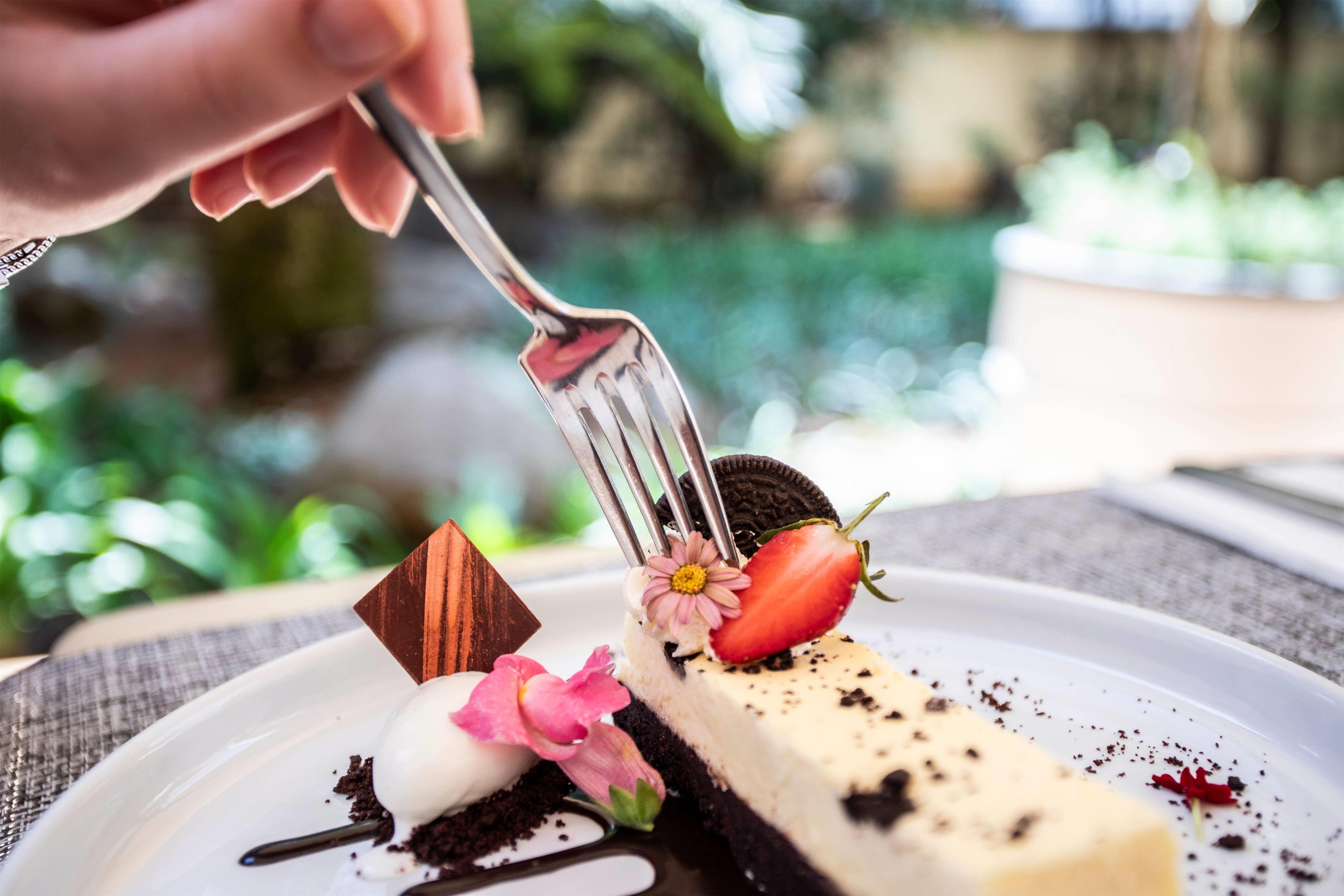 A dessert with a fork, a strawberry, and a flower on a plate.
