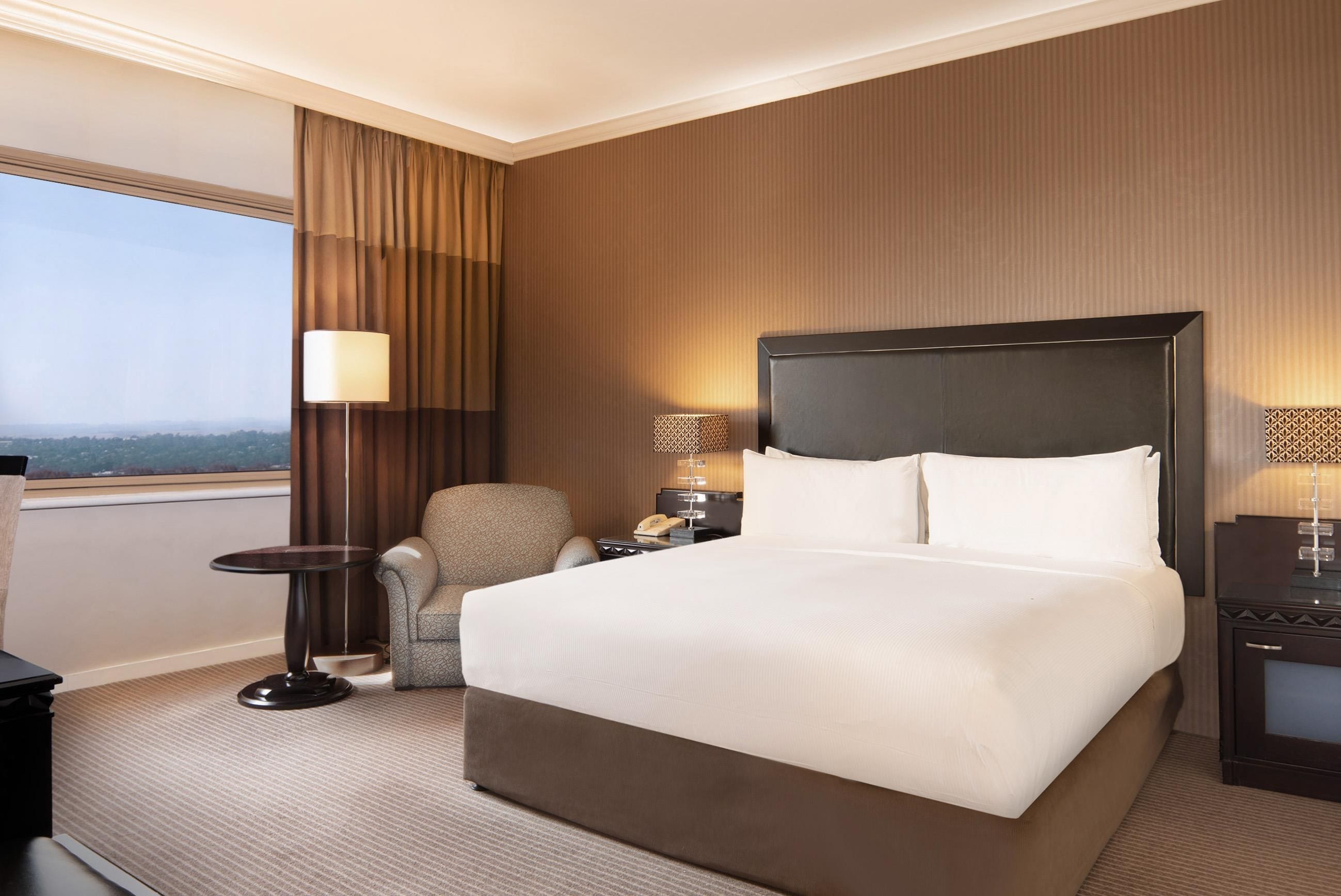 Une chambre d’hôtel avec un grand lit, une chaise, un bureau et une table de chevet avec une lampe.