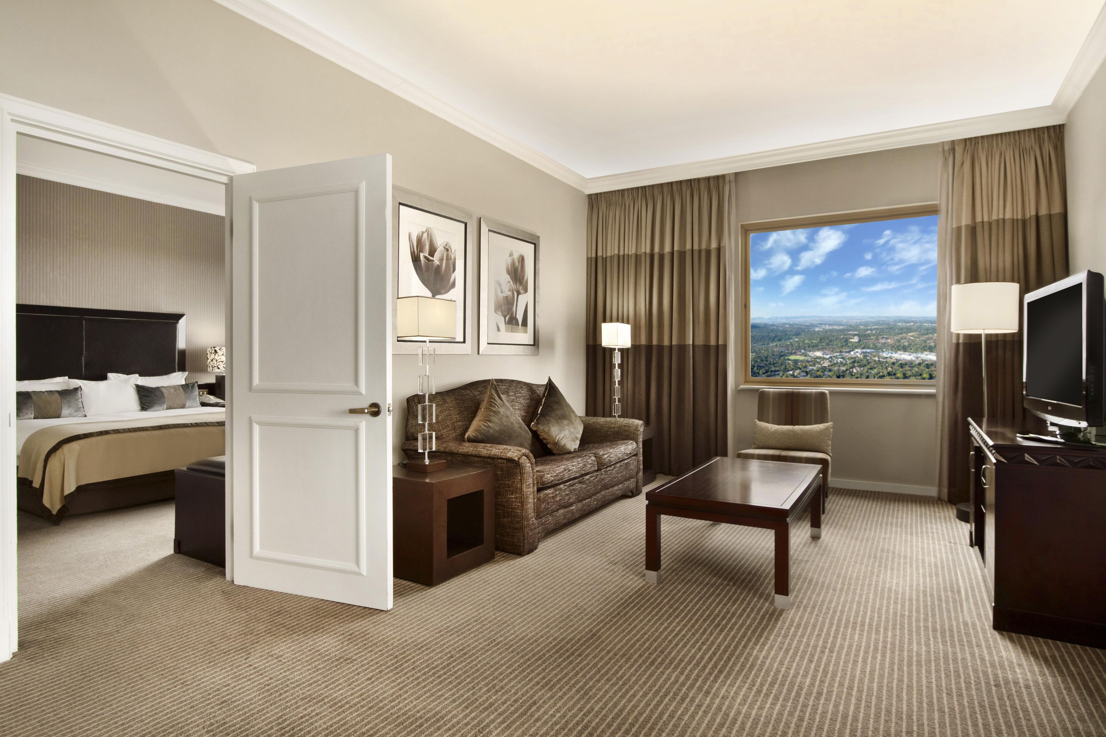 Een hotelkamer met een bed, een bank, een salontafel, een televisie en een raam met uitzicht op de stad.