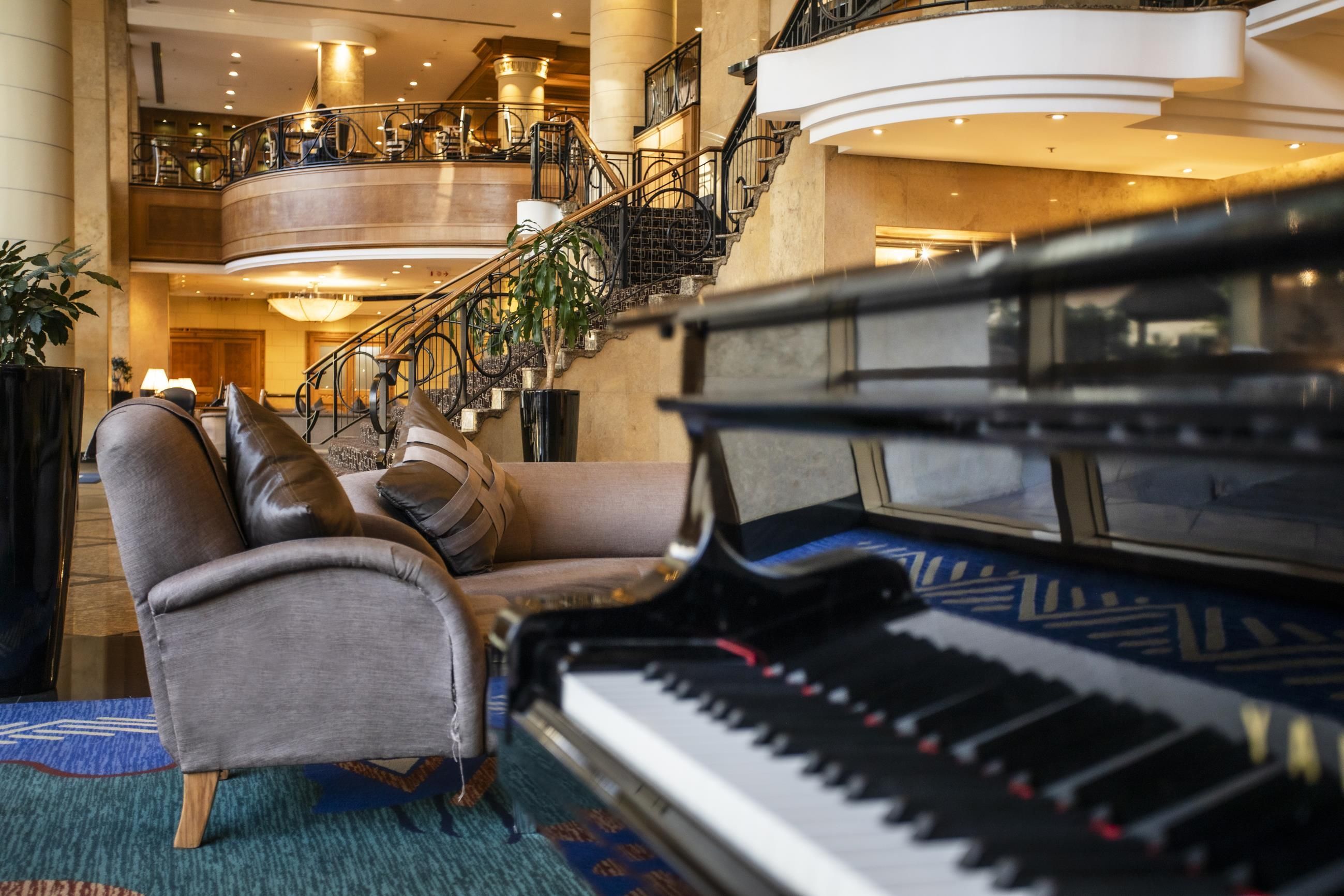 A grand piano in a lobby with a staircase and a seating area.