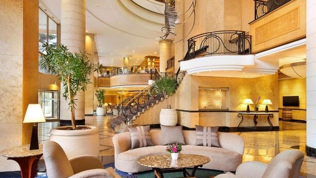 A spacious lobby with a central seating area, a grand staircase, and a large chandelier. - NH Johannesburg Sandton Hotel (Johannesburg)