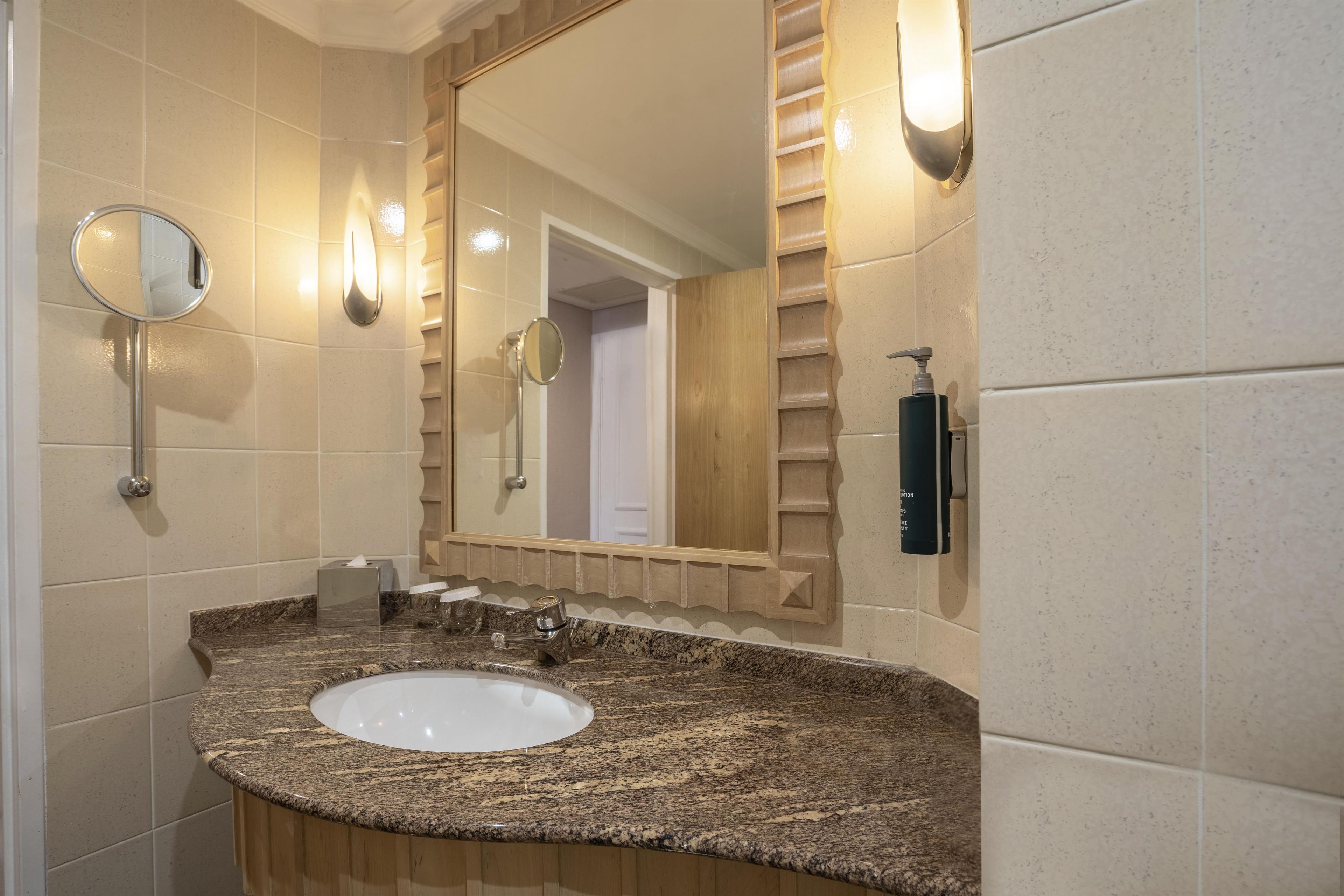 Une salle de bain équipée d’un lavabo avec un plan de travail en granit, d’un miroir, d’un distributeur de serviettes et d’un sèche-mains.