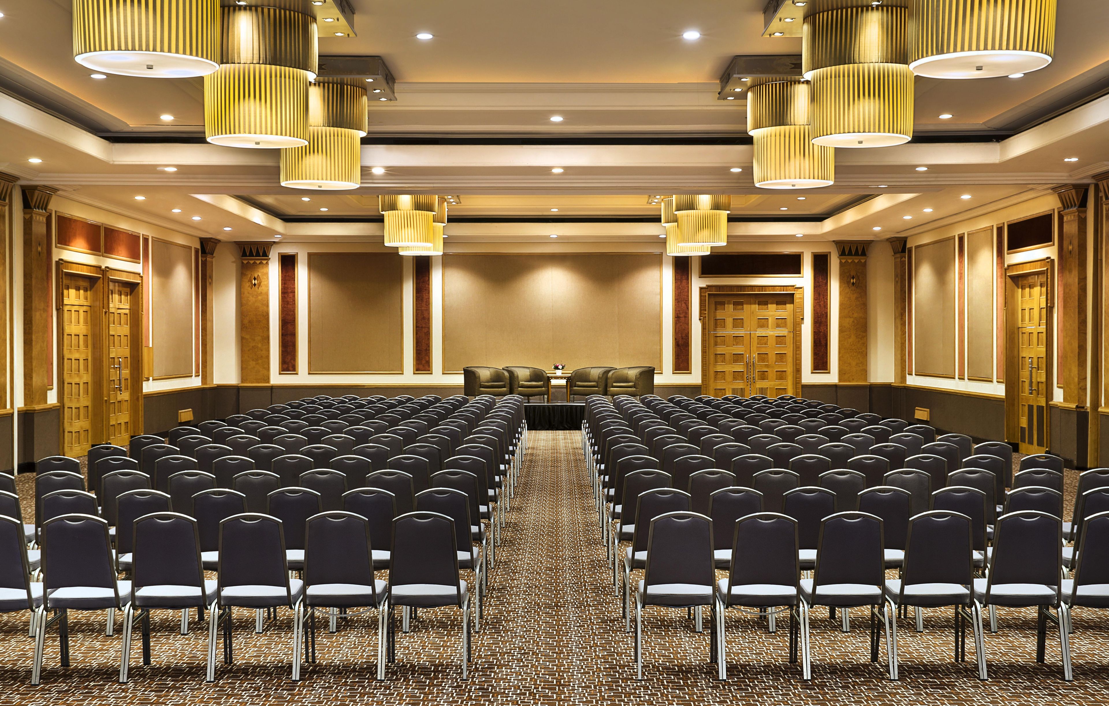 A conference room with rows of chairs, a long table, and modern lighting fixtures.