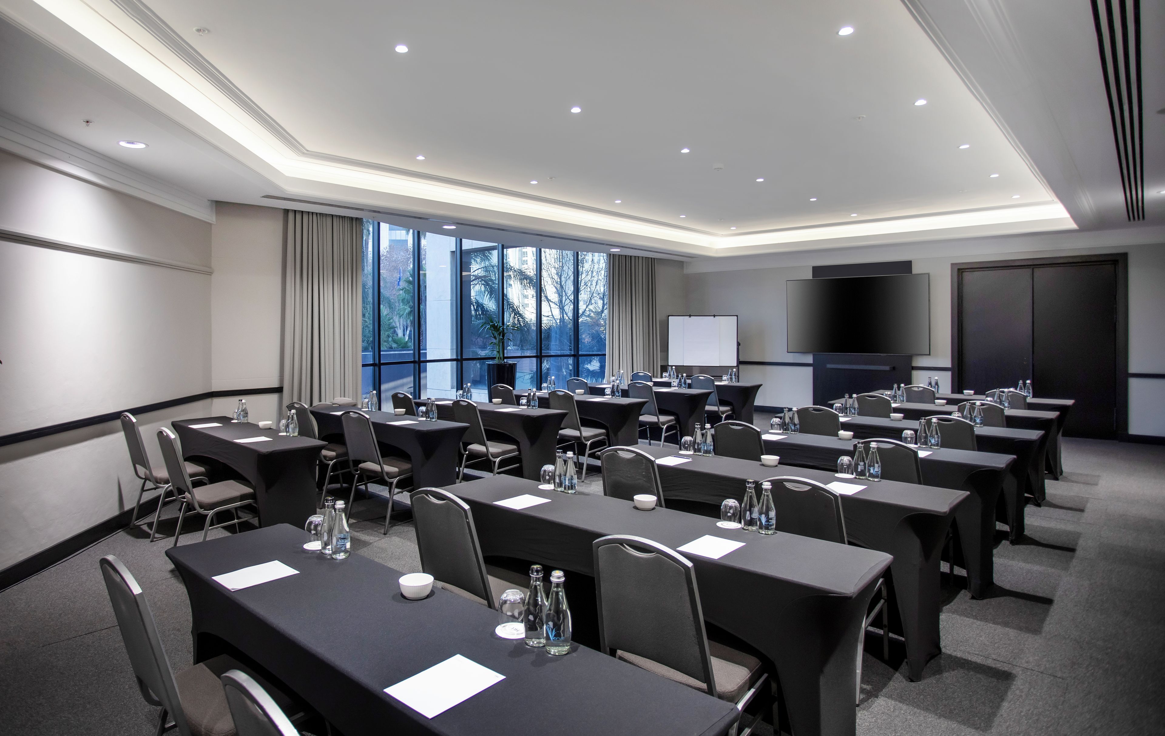 Un salón de conferencias con varias mesas, sillas y una pantalla grande.